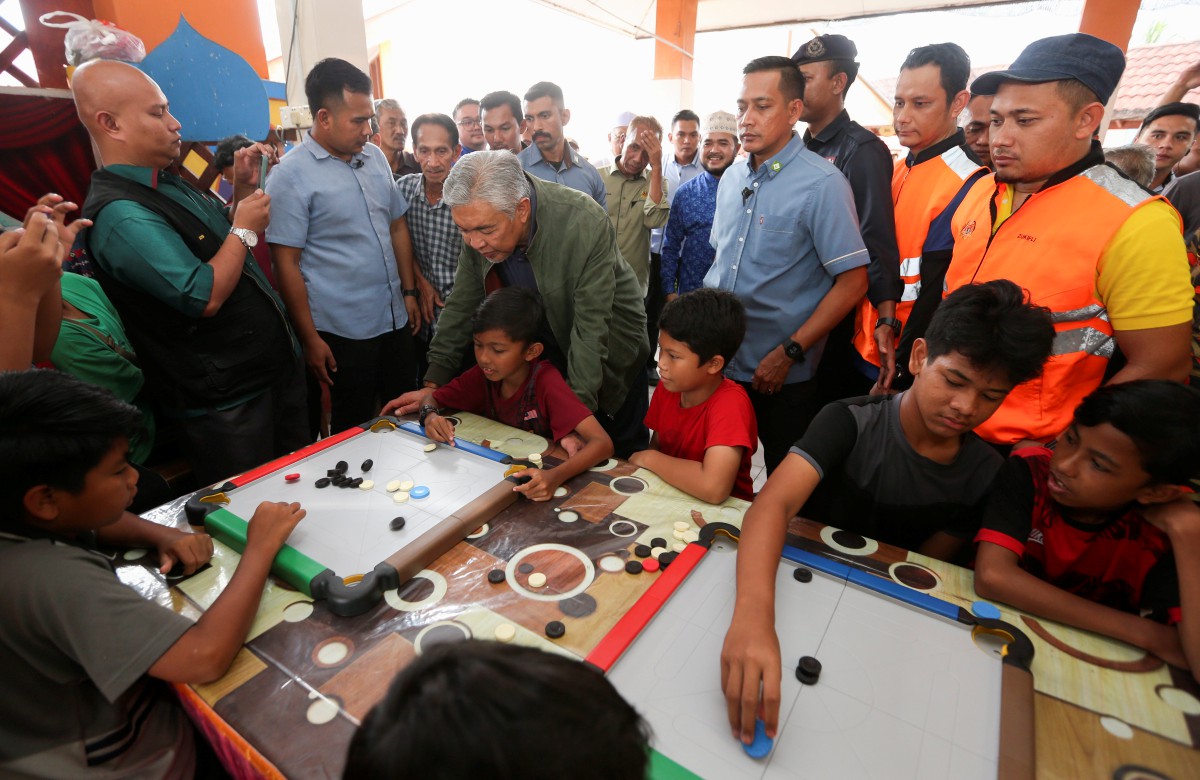 TIMBALAN Perdana Menteri Datuk Seri Dr Ahmad Zahid Hamidi melihat kanak-kanak bermain karom selepas hadir melawat di Pusat Pemindahan Sementara (PPS) di Sekolah Kebangsaan (SK) Jelor. FOTO Nik Abdullah Nik Omar.
