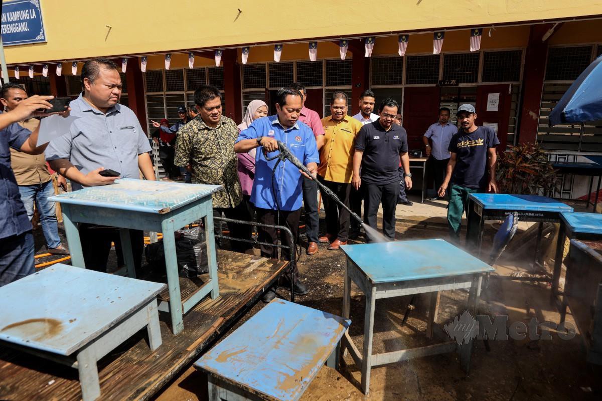 AHMAD Maslan (tengah) mencuci meja sekolah yang dipenuhi lumpur akibat banjir  di SK Kampung La. FOTO Ghazali Kori