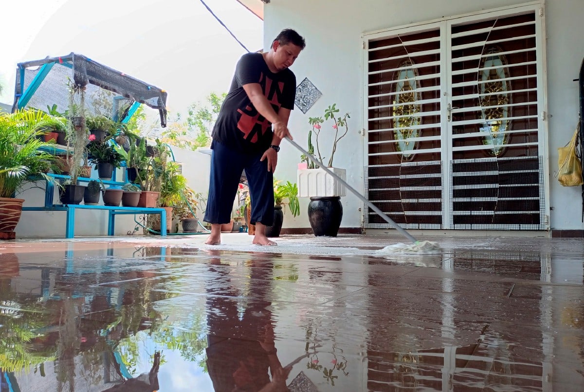 MOHAMAD Sayuti Sudin, 34, membersihkan halaman rumah ibunya yang dinaiki air akibat banjir kilat semalam di Taman Murai Jaya, Durian Tunggal. FOTO Bernama