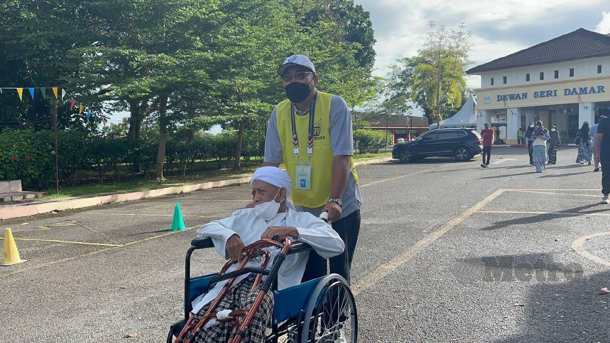 MOHD Jelani dibantu petugas ketika hadir mengundi di Kolej Tingkatan Enam Sultan Sallehuddin Hutan Kampung. FOTO IZAD THAQIF HASSAN