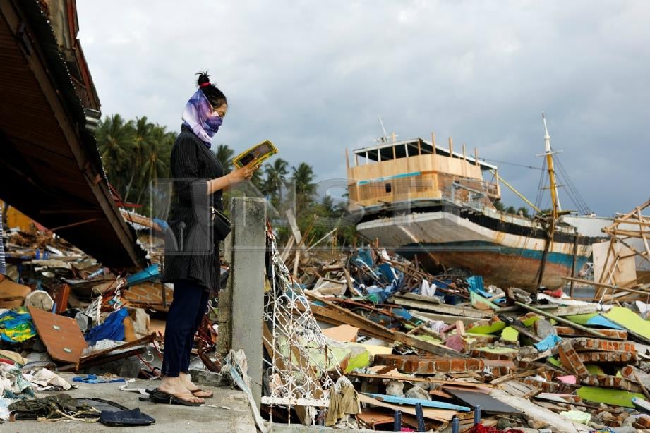 WANITA membaca al-Quran ditemui di celah runtuhan di Palu. FOTO Reuters 