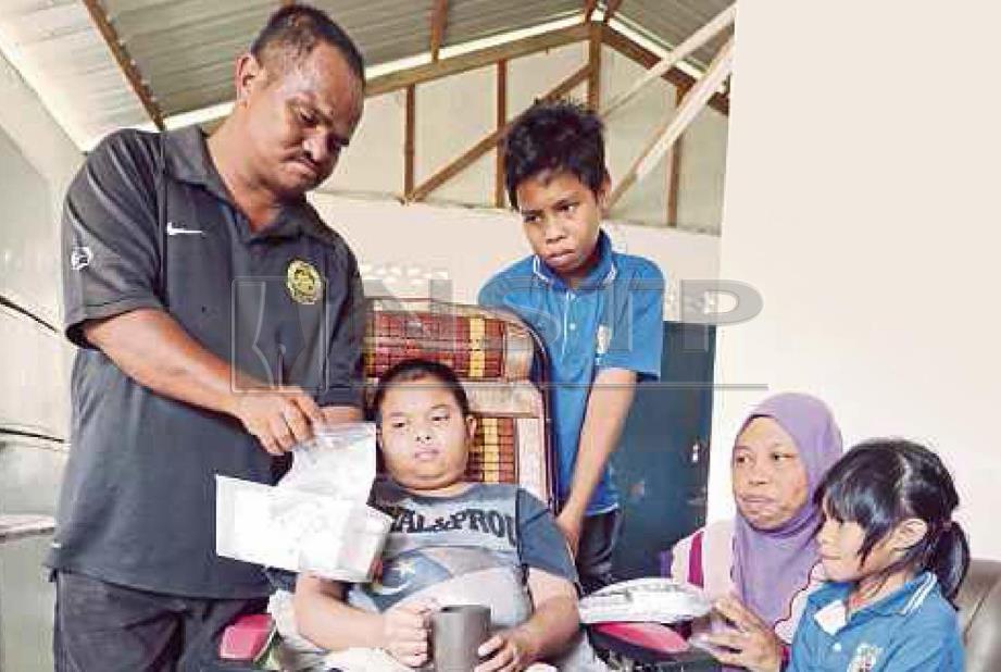 AZLAN (kiri) memberi ubat kepada Muhammad Amirul  (dua dari kiri) yang menghidap tiroid dan ketumbuhan dalam kepala di Jalan Bunga Tanjung, Jasin.