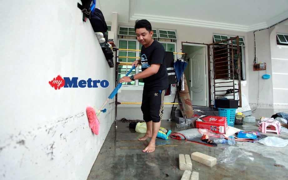 Mohd Syazwan Nazri, 27, membersih kesan kotoran akibat kenaikan air banjir di rumahnya di Taman Pasir Puteh Indah, Pasir Puteh. FOTO Faris Zainuldin 