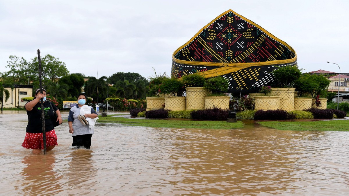 PENDUDUK di sekitar Pekan Donggongan Penampang melintas jalan di bulatan Sigar yang ditenggelami banjir. FOTO BERNAMA