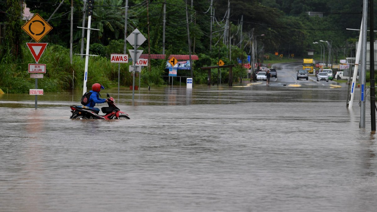 SEORANG penunggang motosikal mengharungi banjir yang menenggelamkan Jalan Kolopis, Penampang hari ini. FOTO BERNAMA