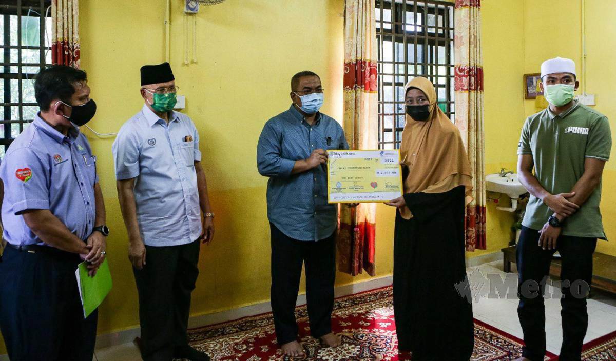 MUHAMMAD Sanusi (tengah) menyerahkan replika cek bayaran faedah sebanyak RM2,000 kepada balu imam Masjid Kubang Jawi, Hafisah di Kampung Lintang, Alor Janggus. FOTO Luqman Hakim Zubir