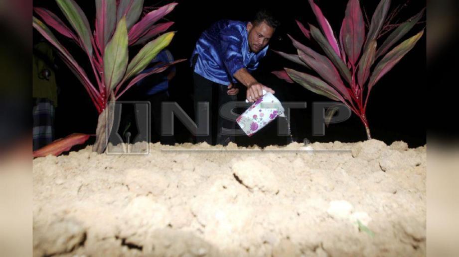 Ibrahim menyiram air mawar diatas pusara Siti Masitah. FOTO Muhd Asyraf Sawal
