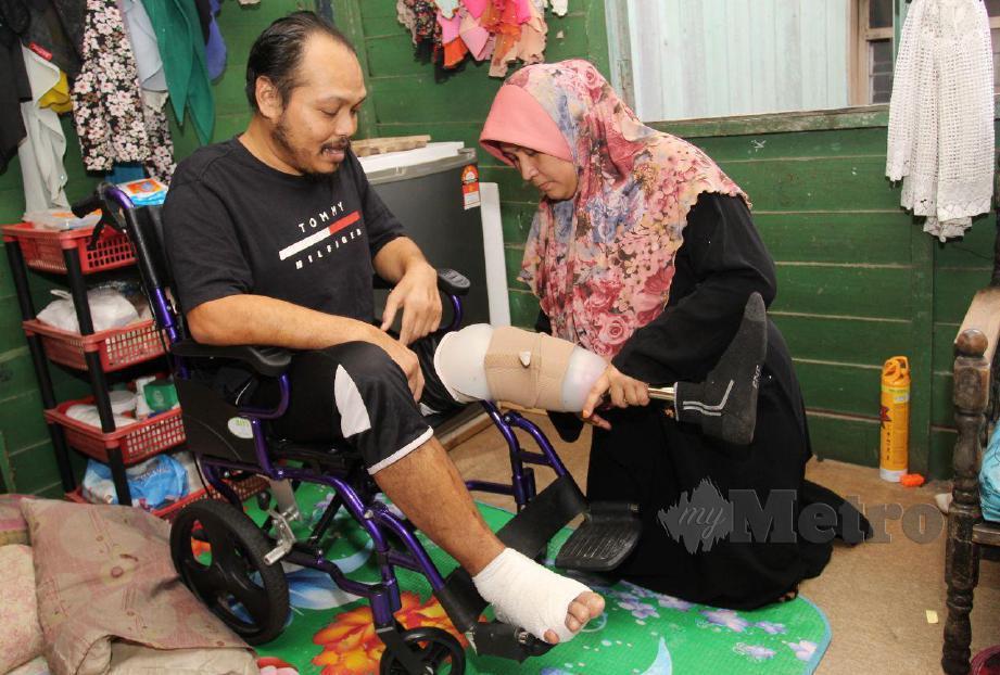 Orang kurang upaya (OKU), Hazrizul Abdul Rahman, 43, dibantu isterinya, Fauziah Ahmad, 37, untuk menguruskan rutin hariannya dengan keadaan kaki kiri yang sudah dipotong sehingga ke paras betis sejak tahun lalu akibat penyakit kencing manis ketika ditemui di rumahnya di Kampung Bukit Tiu. FOTO NIK ABDULLAH NIK OMAR