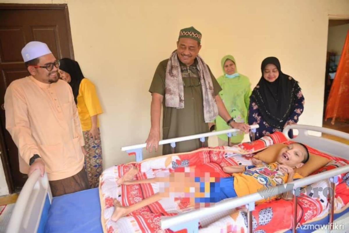 Ab Aziz (tengah) menyerahkan katil khas kepada OKU Mohamad Saifulhafizal dirumahnya di RKT kesedar Sungai Asap B, Gua Musang. FOTO RAMLI IBRAHIM