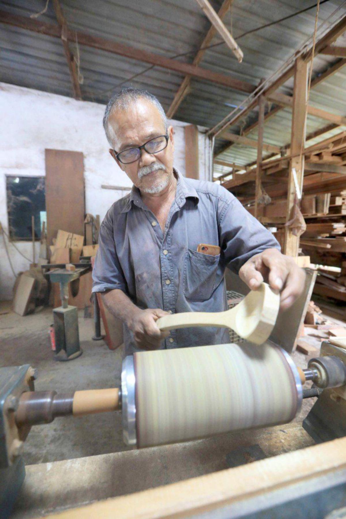 MUHAMMAD menggunakan mesin untuk menghasilkan senduk daripada kayu cengal.