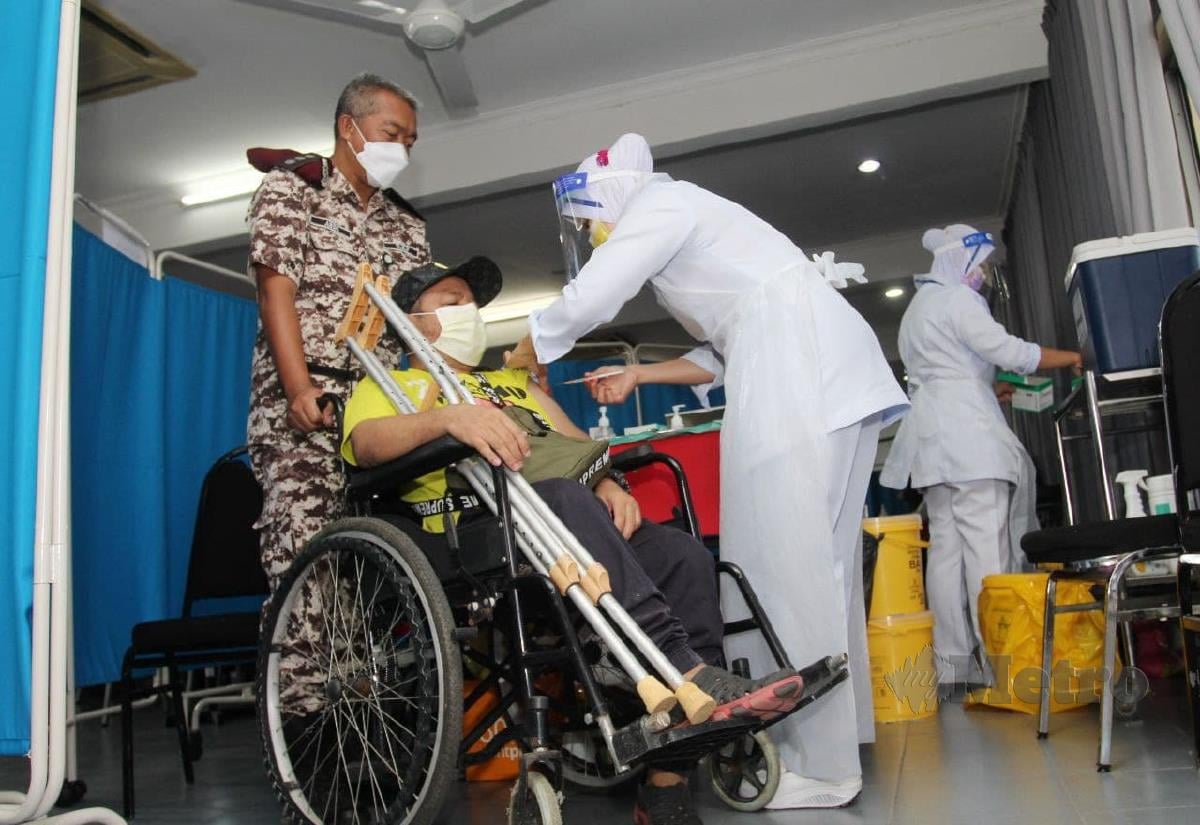 Anggota Penjara Kelantan menolak kerusi roda salah seorang OKU, Mohd Faiza Fauzi, 43, untuk mendapatkan suntikan vaksin. FOTO NIK ABDULLAH NIK OMAR