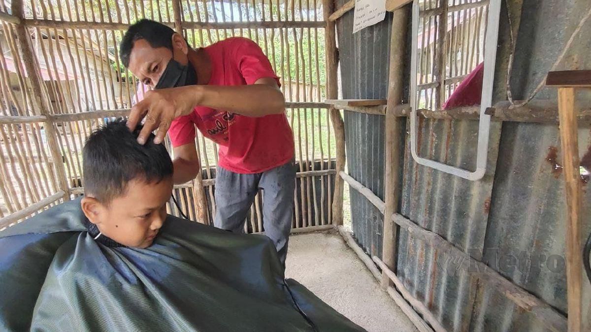 AHMAD Zainun mencari rezeki menggunting rambut di bangsal miliknya yang berdindingkan kayu gelam dan beratapkan zink terbuang. FOTO Syaherah Mustafa