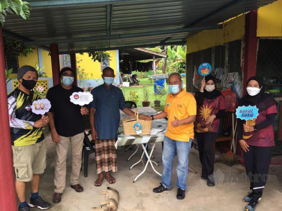 DR Mohd Azlan (dua dari kanan) menyerahkan bakul buku kepada Chaharis di warung makanan perumahan KEDA Teluk Berembang, Pulau Tuba.