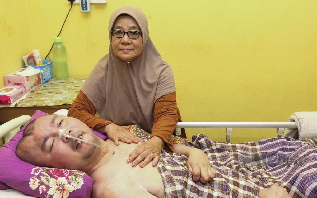 Mek Zah menguruskan anaknya yang berada dalam keadaan separa koma dan terlantar di katil selepas terbabit dengan kemalangan 11 tahun lalu ketika ditemui di rumahnya di Kampung Pangkal Chendok. FOTO NIK ABDULLAH NIK OMAR