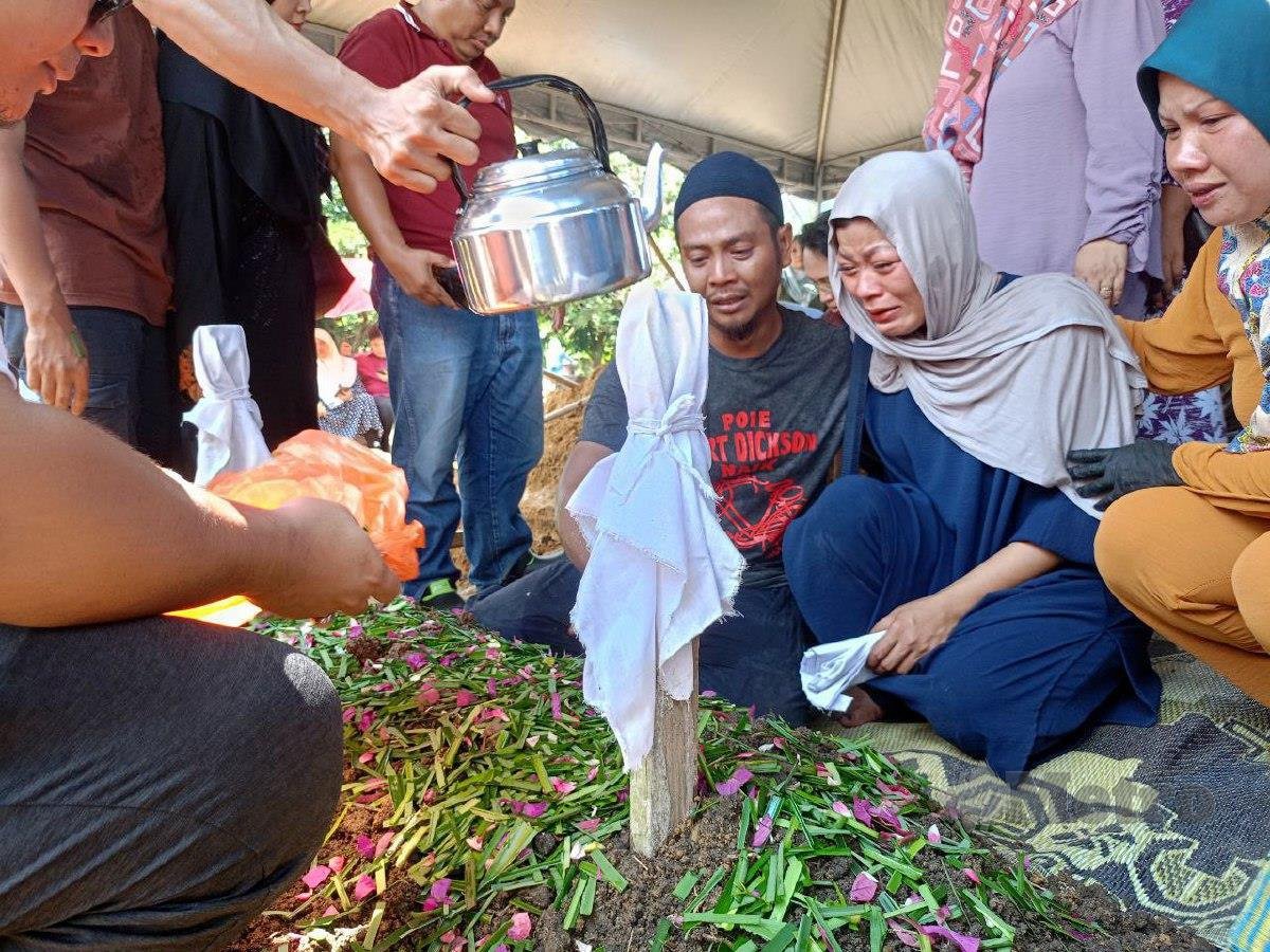 MUHAMMAD Faizal (tengah) memberikan penghormatan terakhir kepada kakaknya, Aszura. FOTO Muhamad Lokman Khairi