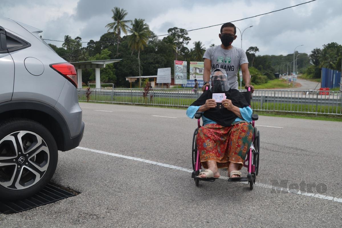 Mohd Yusof menolak kerusi roda dinaiki Pisah selepas menerima suntikan vaksin di Kompleks Sukan Masjid Tanah, Masjid Tanah. FOTO HASSAN OMAR