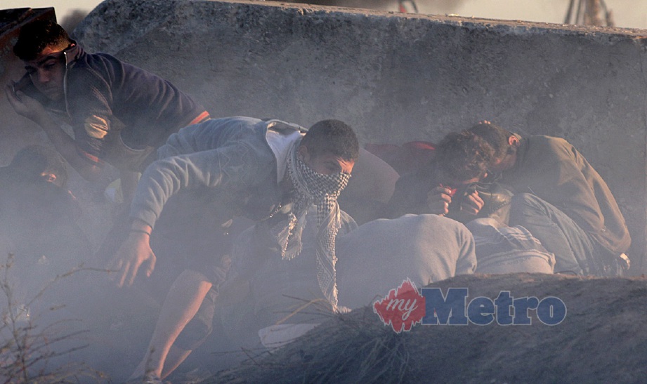 Pembantah Palestin berlindung daripada tembakan tentera dan polis Israel dekat Gaza City, hari ini. - Foto EPA