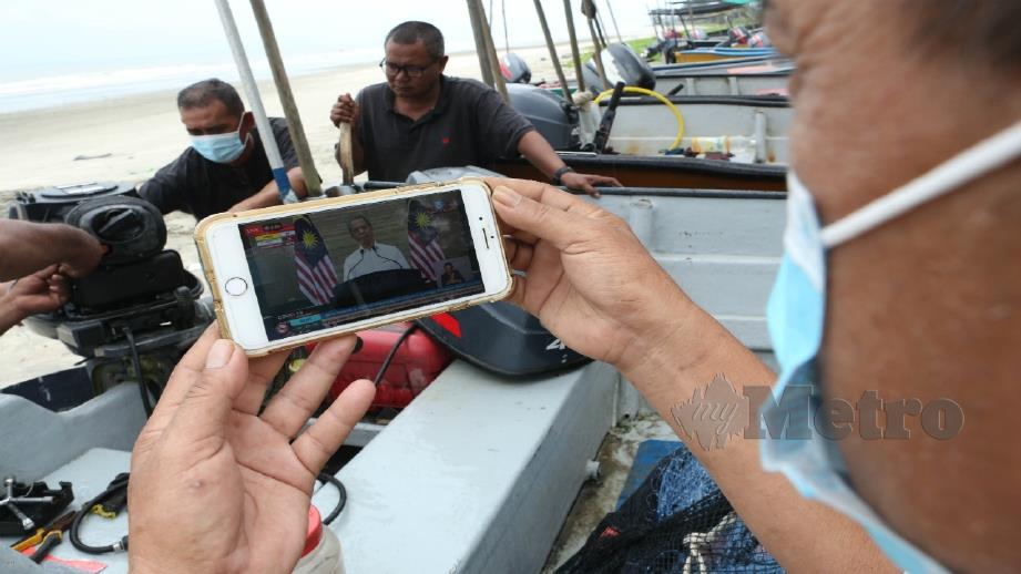 Nelayan pantai menyaksikan perutusan khas Perdana Menteri sempena Hari Pekerja ketika Perintah Kawalan Pergerakan (PKP) di Kuantan hari ini. Foto Farizul Hafiz Awang