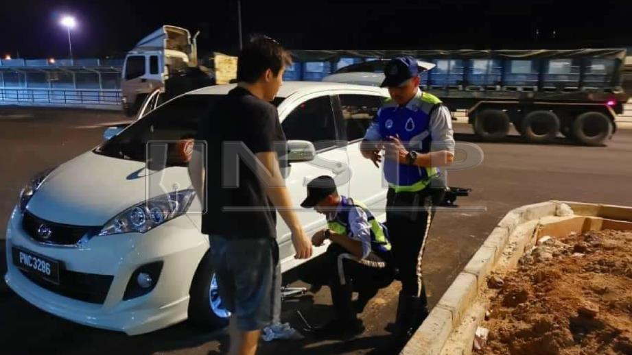 Mohd Arif (berdiri) bersama Mohd Afiq membantu menukar tayar kereta suami isteri. FOTO Ihsan PDRM
