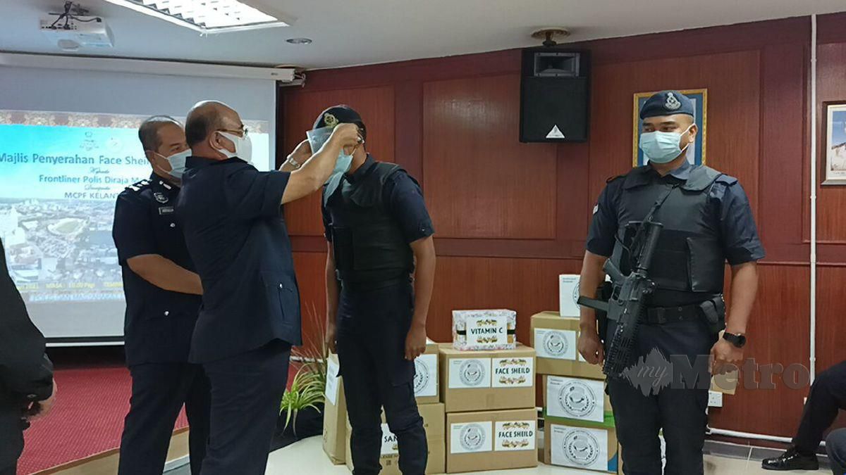 SHAFIEN memakaikan pelindung muka kepada seorang anggota polis sebagai gimik sempena majlis penyerahan pelindung muka dan vitamin daripada MCPF Kelantan kepada PDRM Kontinjen Kelantan. FOTO SITI ROHANA IDRIS