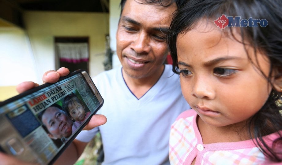 FARHANA  bersama bapa, Rashidi Inou, melihat keratan akhbar digital mengenai kisahnya ketika ditemui di Kampung Tanjung Batu. FOTO Khairull Azry Bidin.