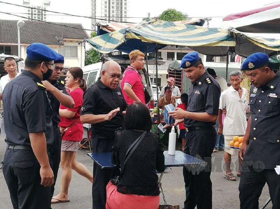 OMAR Ismail (tengah) bersama pegawainya merampas topeng muka yang dijual pada harga berlebihan dalam serbuan di pasar pagi Jalan Teluk Wanjah. FOTO ZULIATY ZULKIFFLI