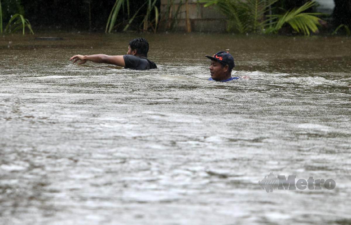 Penduduk meredah banjir untuk menyelamatkan barang-barang selepas halaman rumahnya dinaiki air di Kampung Kubang Kual ke Jalan Kampung Bukit Tandak. FOTO NIK ABDULLAH NIK OMAR