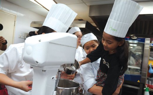 KANAK-KANAK dibantu membuat biskut raya oleh sekumpulan pelajar kulinari Universiti Sunway.