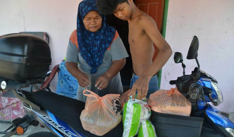 ROBIAH dan anaknya mengangkat barangan makanan disumbangkan penderma di kediamannya di Kampung Bukit Langsat, Tanjung Bidara dekat Alor Gajah. FOTO Hassan Omar
