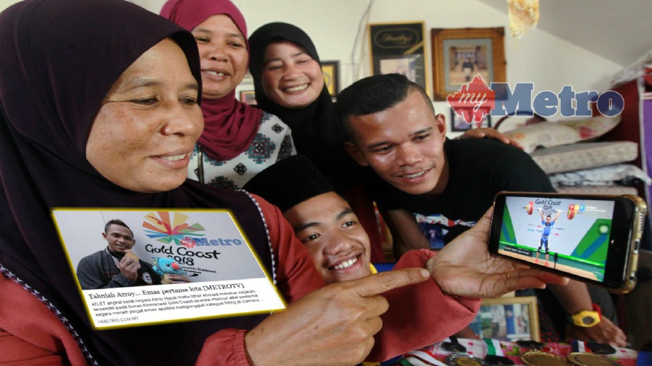 ROHANA (kiri) menyaksikan aksi ulangan Azroy pada acara angkat berat yang memenangi pingat emas pertama Malaysia pada Sukan Komanwel 2018 menerusi telefon pintar di Kampung Sepakat, Rompin, hari ini. FOTO Muhd Asyraf Sawal.