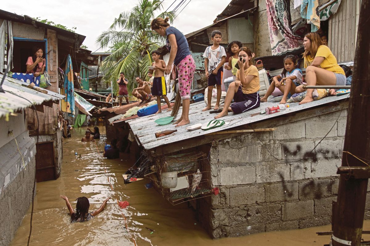 PENDUDUK duduk di atas bumbung sementara menantikan banjir surut di San Miguel, wilayah Bulacan. Ia susulan Taufan Noru di Filipina. FOTO Reuters 