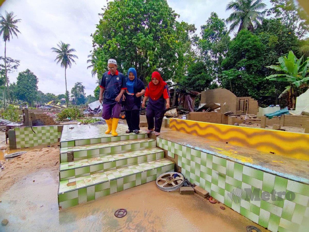 RAJA Kamaruddin bersama anak kembarnya, Raja Syahirah dan Raja Nursyafiqah melihat rumah mereka yang hilang dibawa arus deras di Kampung La. FOTO Nurul Fatihah Sulaini