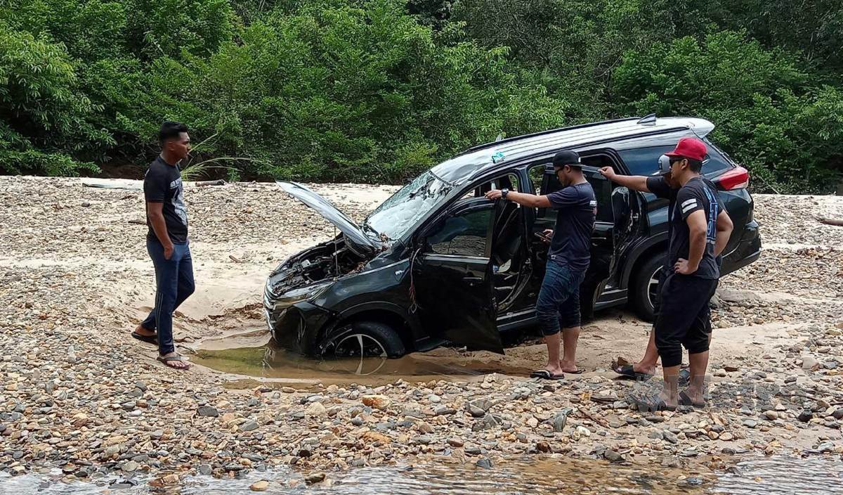ROSLAN (kiri) bersama rakannya melihat kereta jenis Perodua Aruz dihanyutkan arus sejauh kira-kira satu km daripada kawasan tempat letak kereta dalam kejadian kepala air di Ulu Kasar, Lata Payung, Setiu. FOTO Baharom Bakar