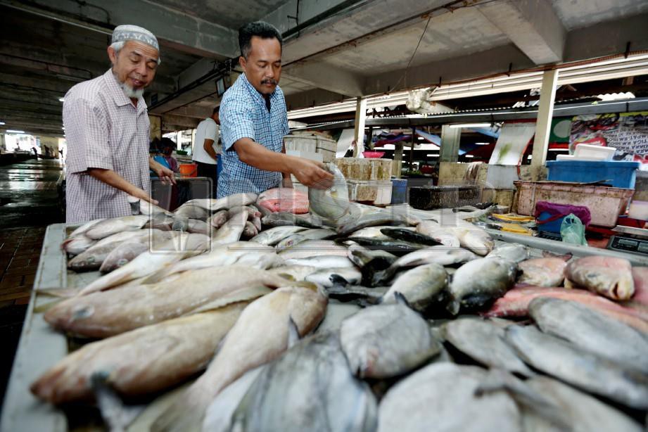 ASRI  (kanan) melayan pelanggan membeli ikan  di gerainya. -Foto IMRAN MAKHZAN 