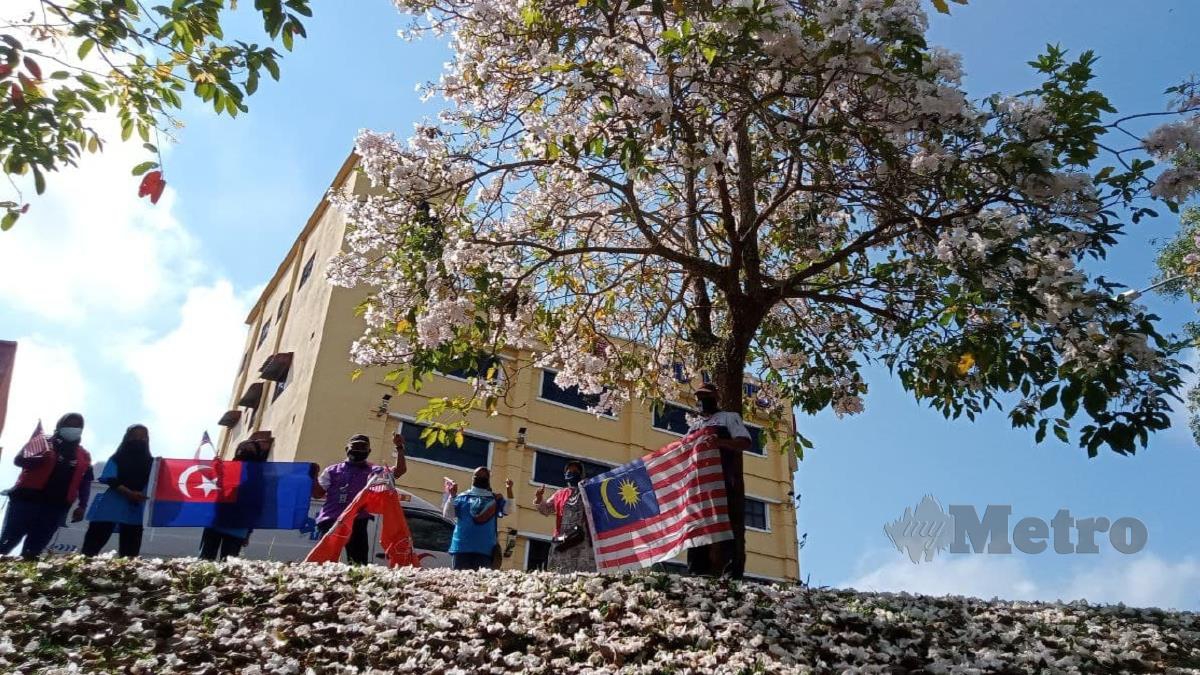 FAIRUZ (tiga kanan) bersama sukarelawannya merakamkan gambar musim Sakura bersama Jalur Gemilang dan bendera Negeri Johor di bandar Segamat. FOTO Ahmad Ismail.