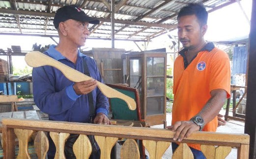MOHD Fadli (kiri) berbincang dengan seorang pekerja bagi menghasilkan barangan daripada kayu pain terpakai.