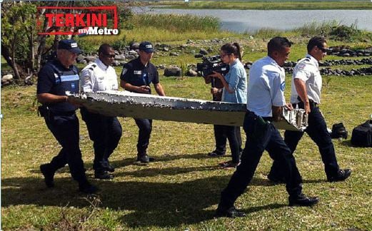 Anggota polis mengangkat objek dipercayai serpihan pesawat daripada MH370. FOTO AFP