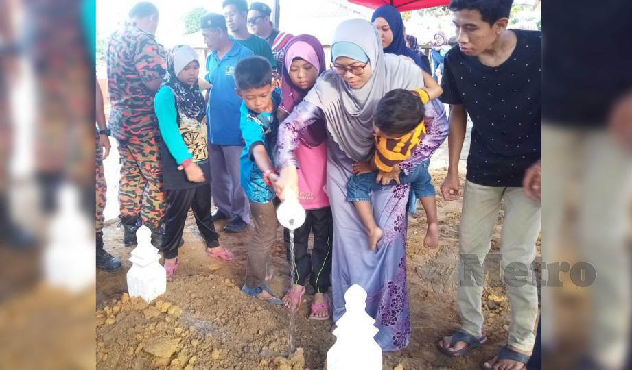 SITI Hawa bersama tiga anaknya menyiram air mawar pada pusara suaminya Mohamad Haitimi selepas dikebumikan di Tanah Perkuburan Islam FELDA Penggeli Timur. FOTO Adnan Ibrahim