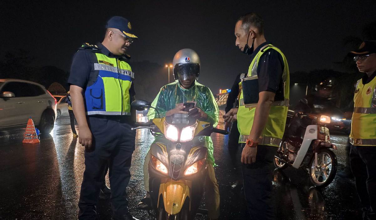 Firdaus (kiri) memeriksa lesen pengguna jalan raya pada Operasi Khas Hari Raya Aidiladha (HRAA) di Lebuh Alor Gajah-Melaka Tengah-Jasin (AMJ) Bukit Piatu lewat malam tadi. FOTO Bernama