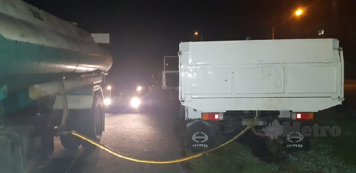Kegiatan seorang lelaki yang cuba memindahkan diesel dari sebuah lori ke lori lain dengan menggunakan dua hos, malam tadi. FOTO ERIKA GEORGE