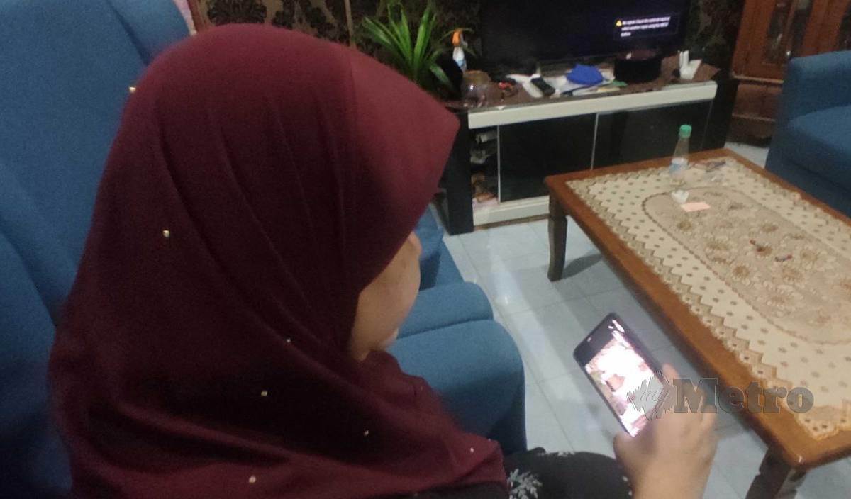 ANIMAH melihat rakaman video pengkebumian jenazah abangnya, Mohd Fazil yang meninggal dunia akibat Covid-19 menerusi telefon pintarnya di rumahnya di Kampung Pengadang Baru. FOTO Zaid Salim