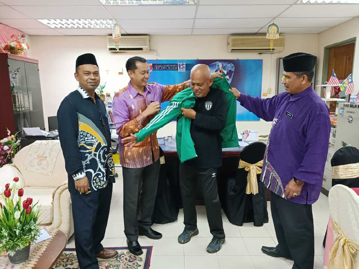 Azahari Salim (dua kanan) dipakaikan baju sukan Piala Dunia 2022 oleh Penolong Pengarah,Unit Pembangunan Bakat Murid (MSST), Jabatan Pendidikan Negeri Terengganu, Hamdan Awang di SMK Seri Nilam, semalam. FOTO ihsan Hamdan Awang