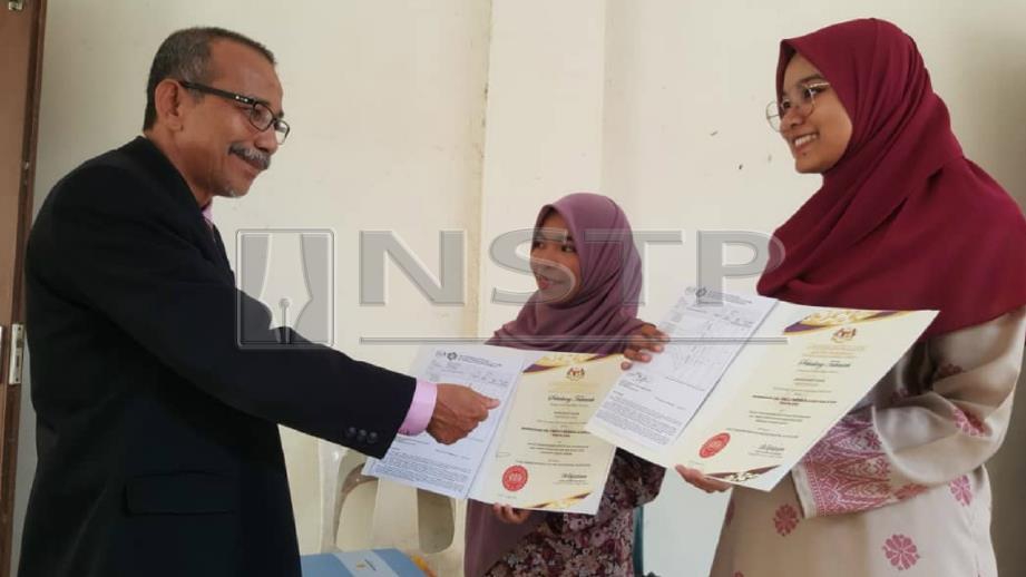 Asma ( kiri) dan Amisya menunjukkan slip keputusan dan sijil kecemerlangan yang diperolehi kepada Pengetua SMK Tunku Putra. FOTO Hamzah Osman