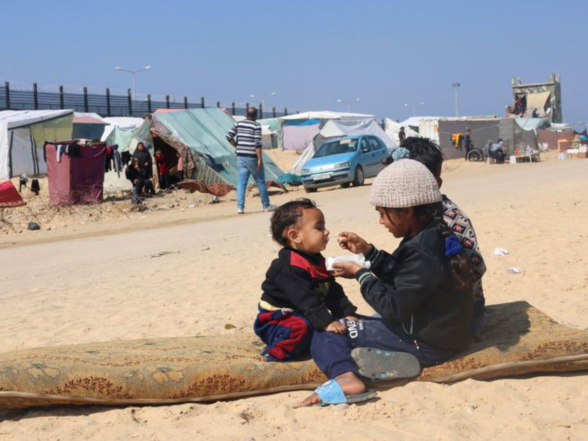 KANAK-kanak perempuan memberi adiknya makan di sebuah kem berhampiran Mesir di Rafah. FOTO Reuters