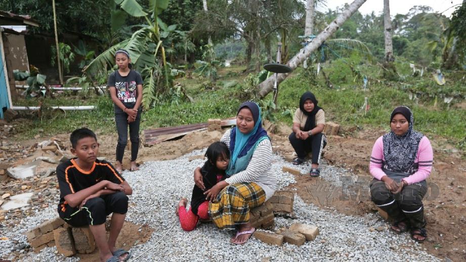 SURIATI (tengah) bersama empat anak dan adiknya kelihatan sugul di tapak rumah mereka selepas kediaman mereka dihanyutkan banjir. FOTO Ghazali Kori