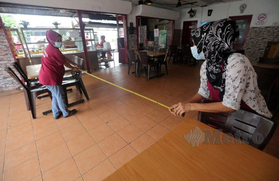 PENGUSAHA restoran, Hanis Bahari, 46, mengukur jarak susunan meja bagi membuat persiapan membuka kembali perniagaannya di Taman Desa Bukit Permata, Kapar. FOTO Muhd Asyraf Sawal