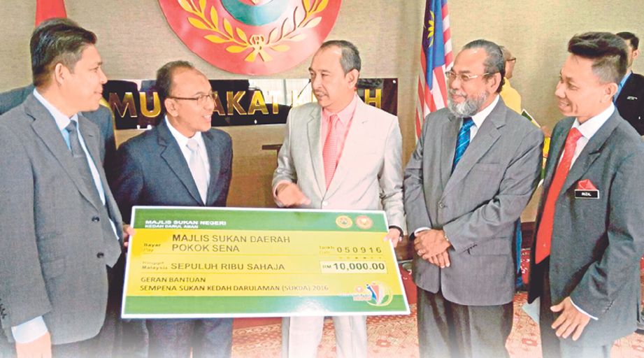 AMINUDDIN (tengah) menunjukkan geran bantuan kepada wakil kontinjen daerah di Kedah sempena penganjuran SUKDA.