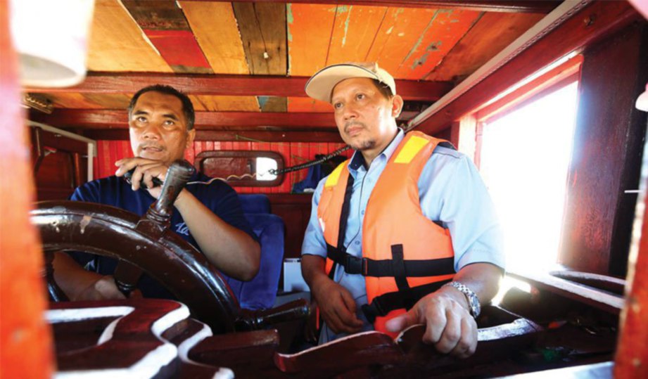 HAZAHAR (kiri) dan Mohd Zin menunjukkan cara penggunaan radio di dalam bot nelayan.
