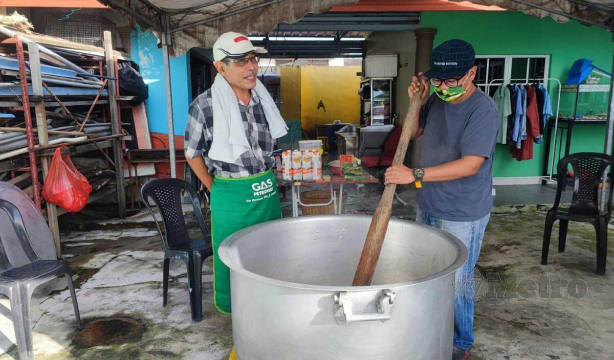 TOK Banang (kiri) dibantu menantu, Khairul Aime ketika memasak bubur lambuk bagi memenuhi tempahan. FOTO Mary Victoria Dass