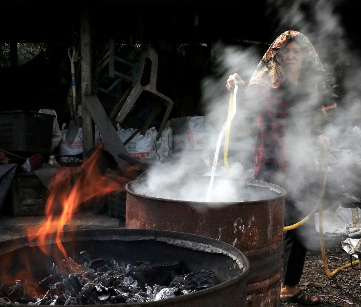 PROSES pemadaman api pada kelapa yang dibakar di dalam tong untuk dijadikan arang.